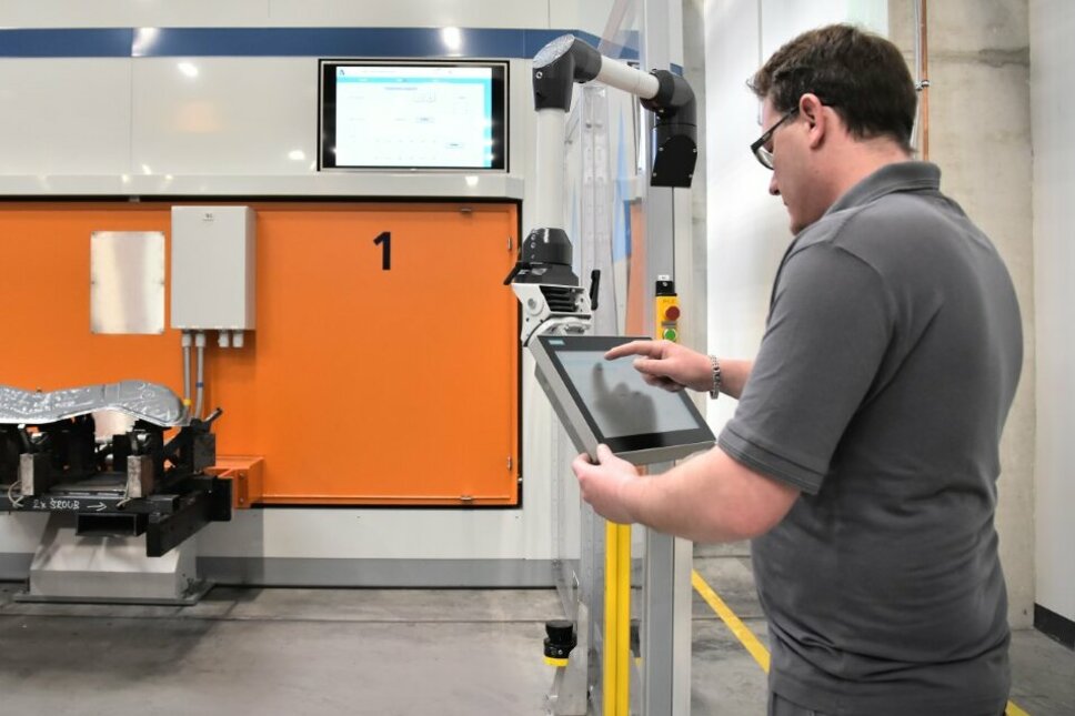  A laser technician is programming the laser cutting machine visible in the background using a tablet.