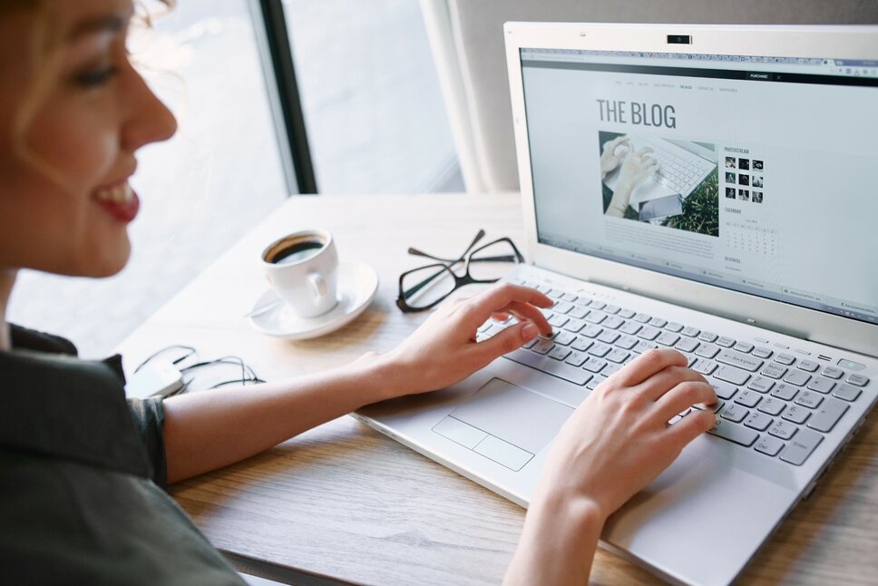 Foto einer Frau, die konzentriert an einem Laptop arbeitet. Auf dem Bildschirm des Laptops ist deutlich "The Blog" zu sehen, was darauf hindeutet, dass sie entweder an einem Blogbeitrag schreibt oder Bloginhalte durchstöbert.
