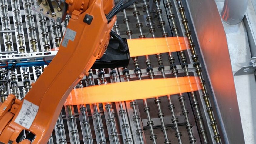 Industrieller Roboterarm in der Prozesstechnik für das Presshärten positioniert glühend heiße Metallbleche auf einer Produktionsanlage. Der Einsatz modernster Technologie optimiert den Presshärteprozess und gewährleistet eine präzise Steuerung der Umformprozesse bei weba Werkzeugbau.