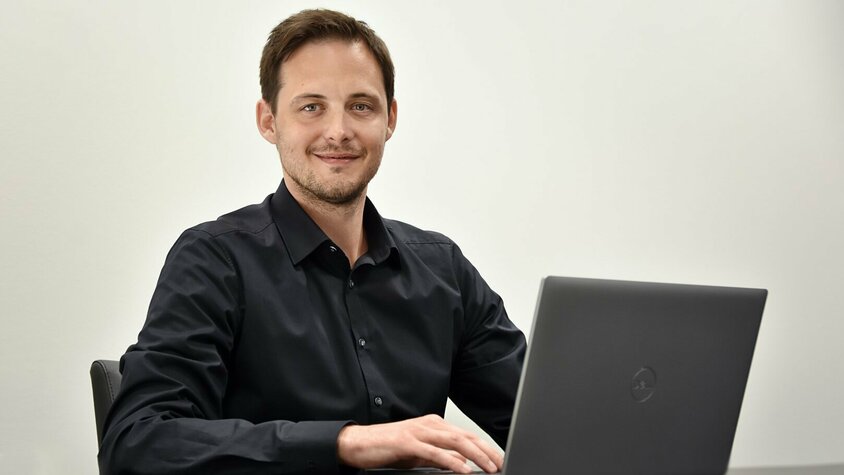 Ondrej Zima, Human Resource Manager der weba Olomouc sitzt avor einem geöffneten Laptop und  lächelt in die Kamera