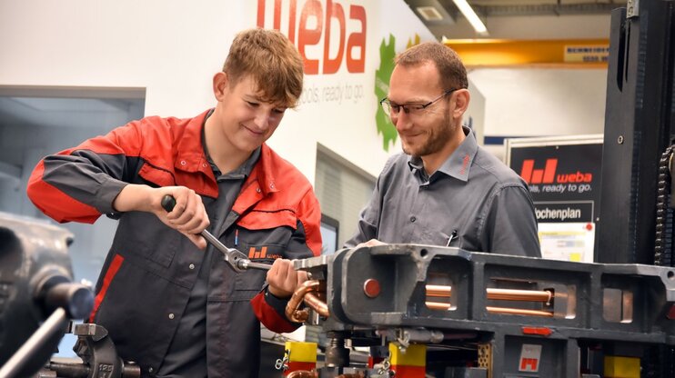 Ein Lehrling in der Werkzeugbautechnik arbeitet an einer Miniatur eines Umformwerkzeugs, während der Ausbilder aufmerksam zuschaut. weba Werkzeugbau bietet Lehre in Steyr in der Metalltechnik an.