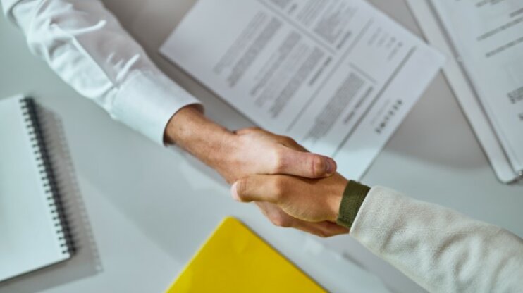 Shaking hands after a successful agreement over signed contracts. The image symbolizes the signing of a contract for a career change.