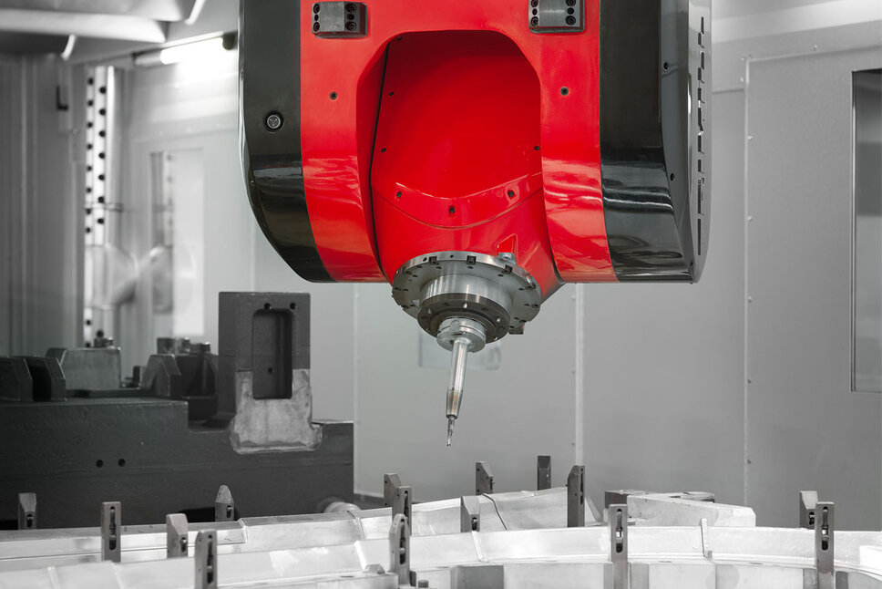 Close-up of a CNC machining head during a milling operation in mechanical machining. The red and black milling head is precisely positioned over a clamped workpiece. The sharp cutting tip of the tool is ready for high-precision machining to mill complex shapes into the material. In the background, the interior of the CNC machine is visible, indicating a controlled and professional production environment.