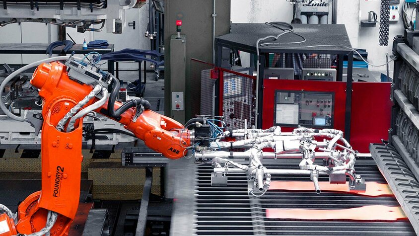 Roboter-Arm entnimmt zwei glühende Formplatinen für den Transfer in die Warmumformpresse