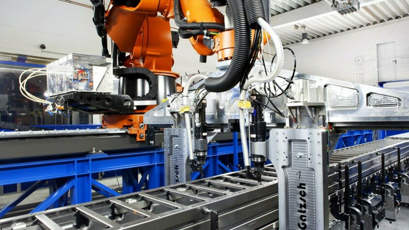 Ein moderner Industrieroboter in einer Produktionshalle, der an einer automatisierten Fertigungslinie arbeitet. Der Roboter führt Nieten und Clinchen durch, um Metallkomponenten präzise zu verbinden. Die Anlage ist an einer Förderanlage befestigt und befindet sich in einer hellen, industriellen Umgebung, die für effiziente und präzise Prozesse in der Fügetechnik steht.